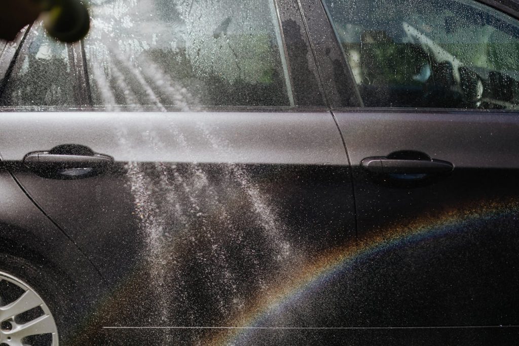 Close-up of a car being washed with a visible rainbow in sunlight.