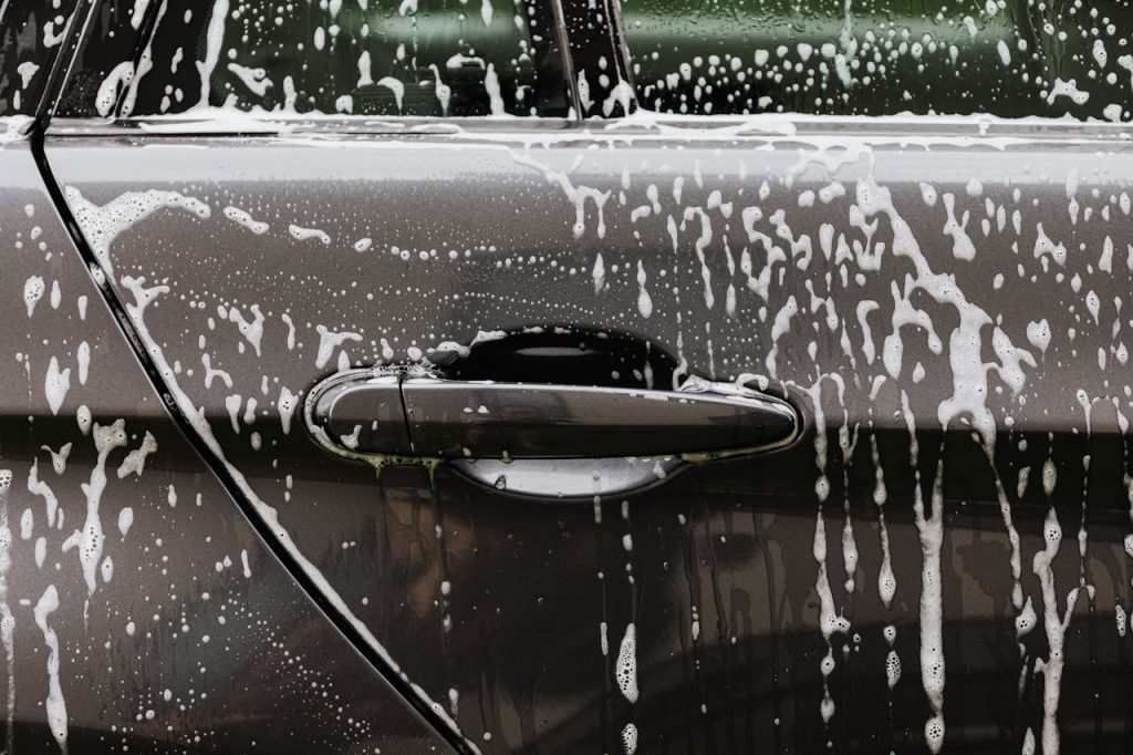 Detailed close-up of soap suds on a black car door during a wash, highlighting automotive care.